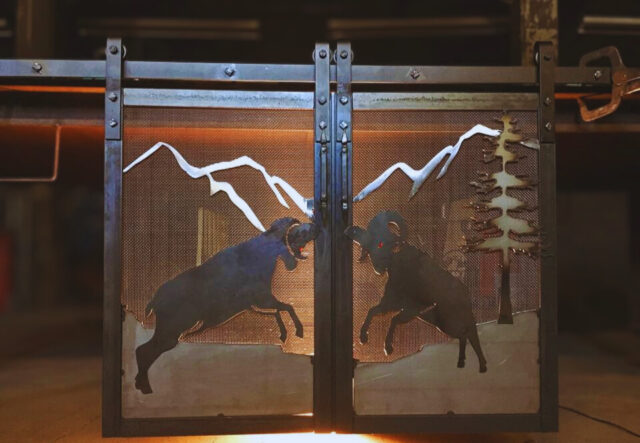 Rolling metal fireplace doors custom made by Antietam Iron Works with a mountain scene including big horn sheep with glass eyes